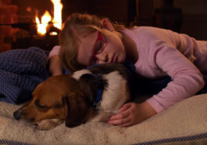 Little girl and adopted dog cuddling in front of flireplace